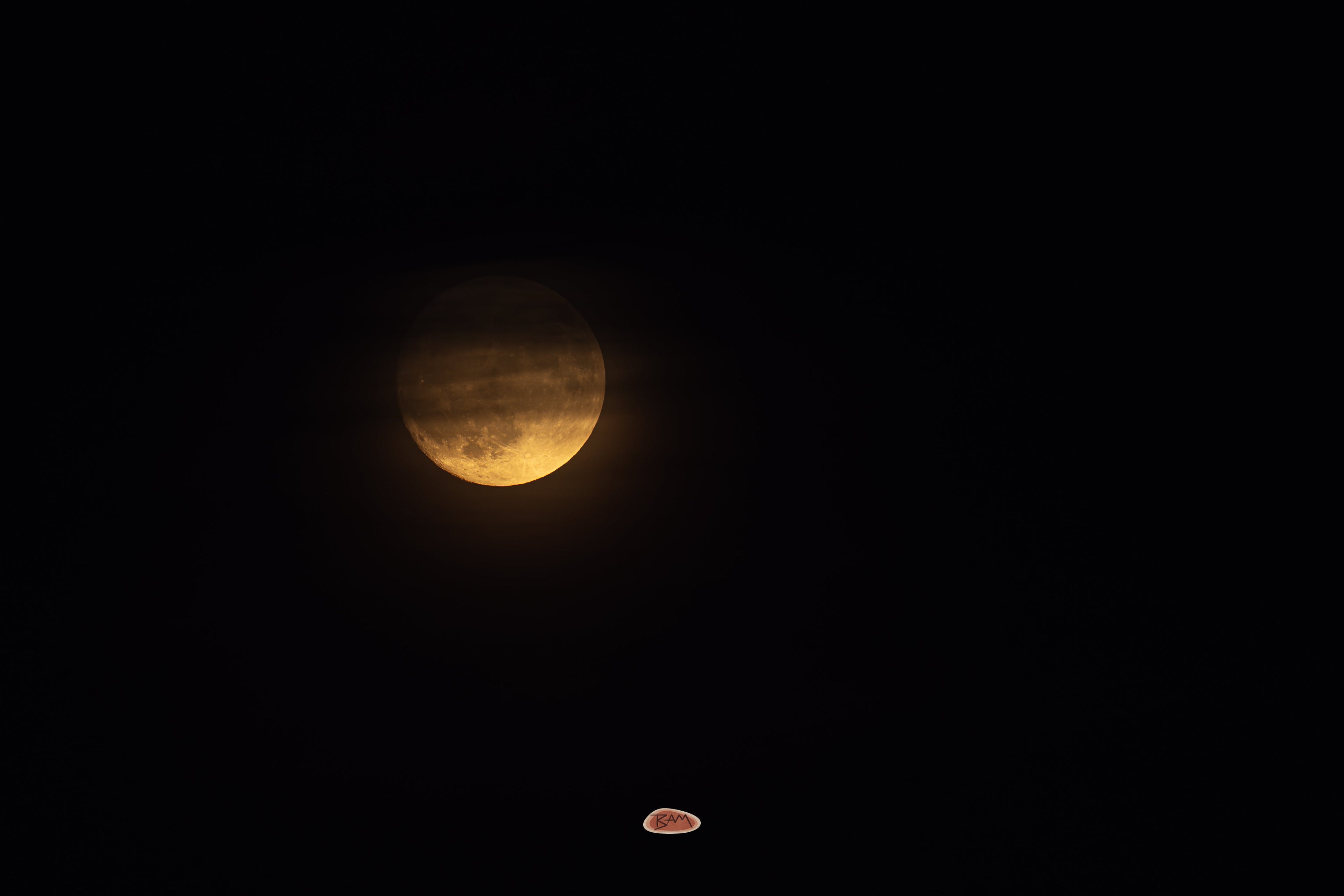 Moon Glowing amber moon partly veiled by haze in a black night sky